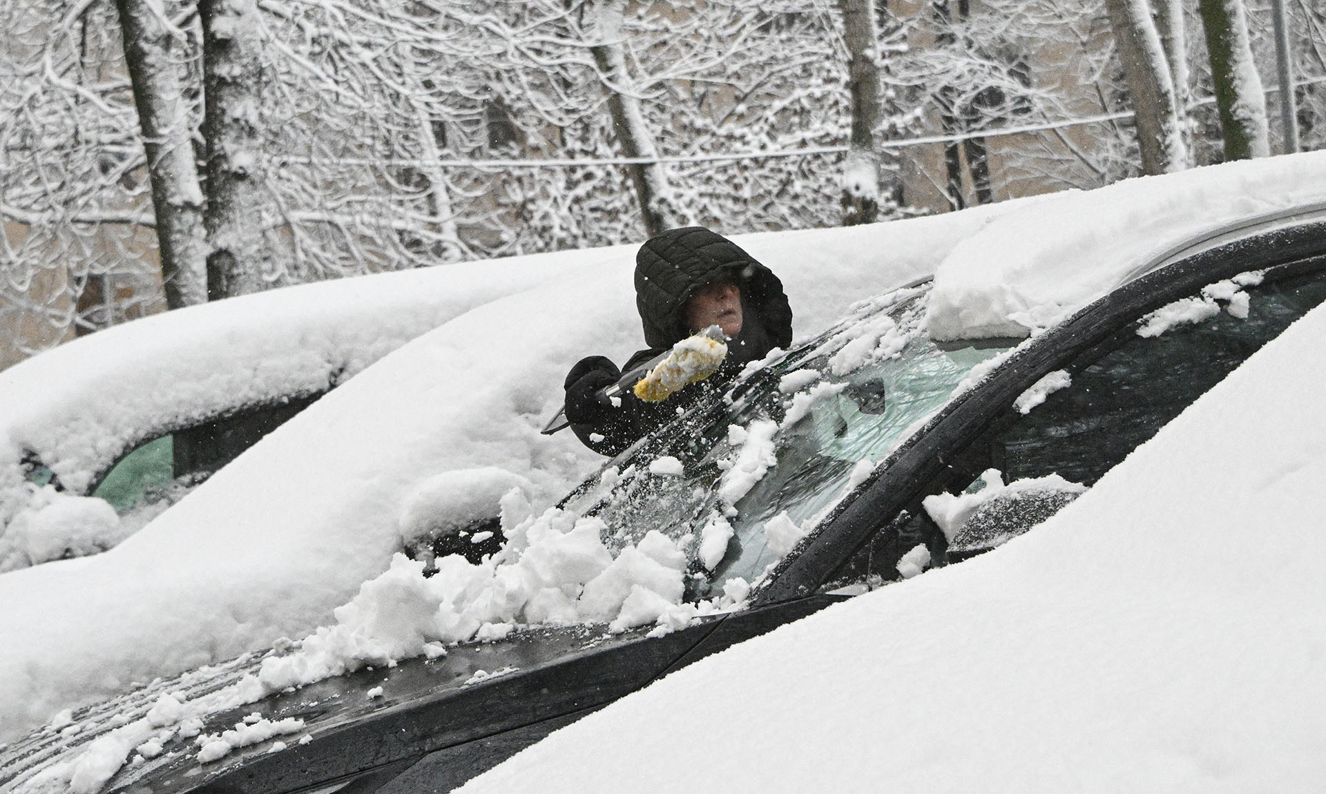 Женщина очищает машину от снега