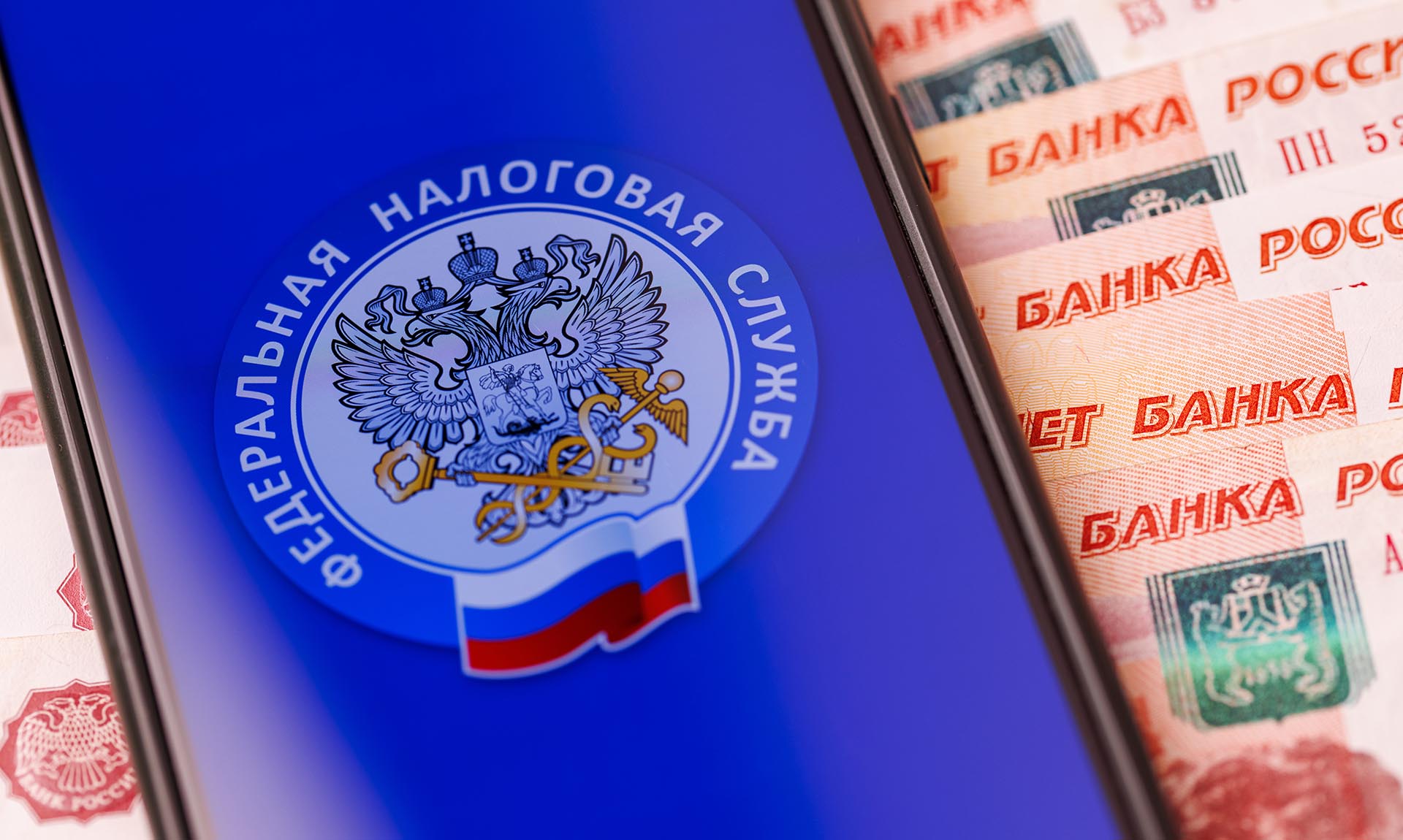 Эмблема ФНС на экране смартфона и пятитысячные купюры
