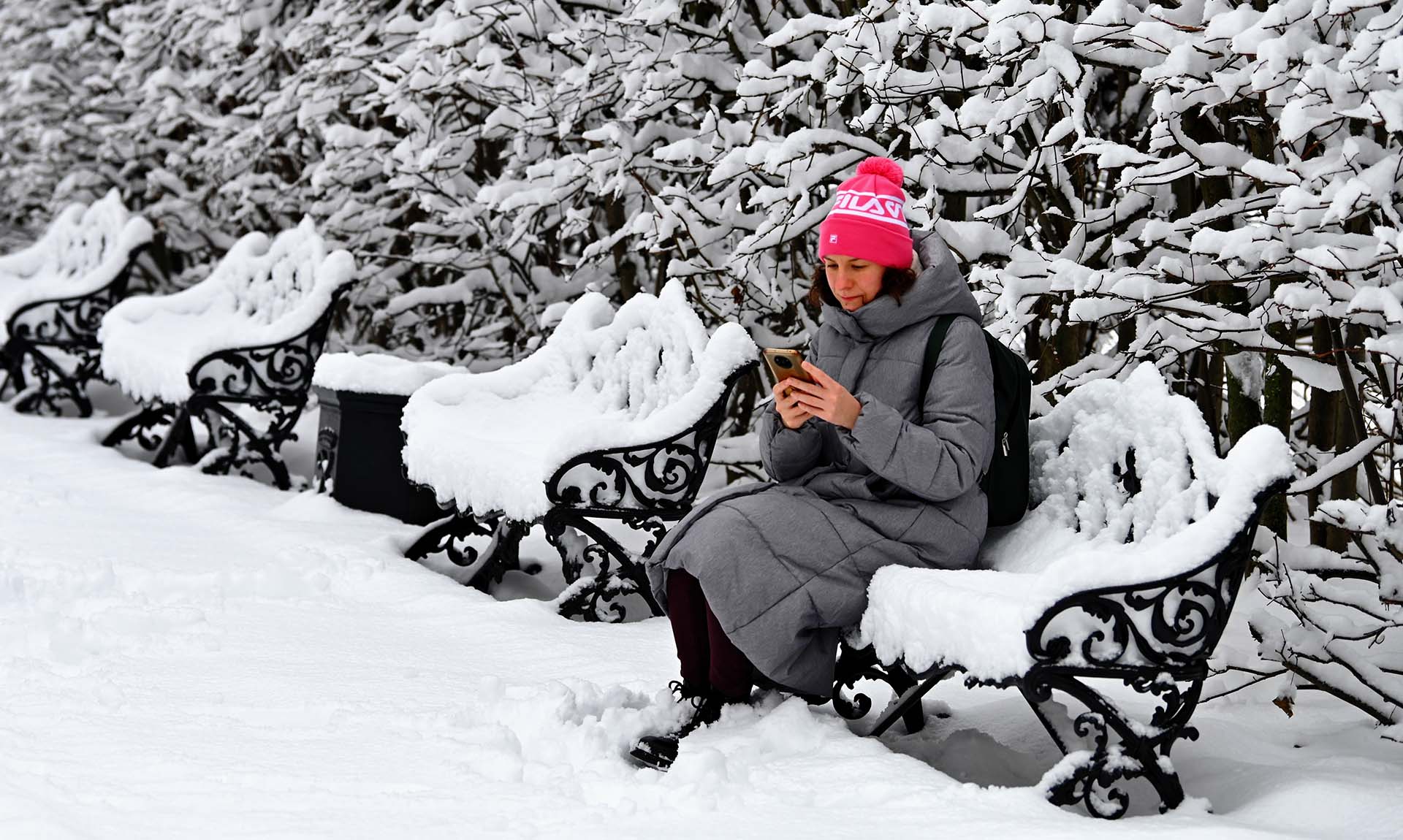 Женщина с телефоном сидит на скамейке в парке 