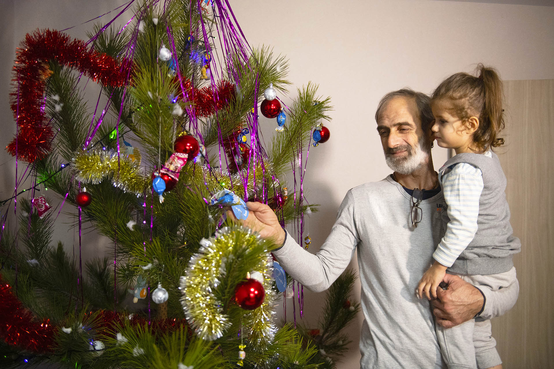 мужчина с ребенком на руках украшает елку