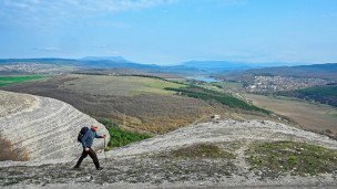 Турист на пешем маршруте на фоне видно водохранилище и город, вокруг туриста холмы