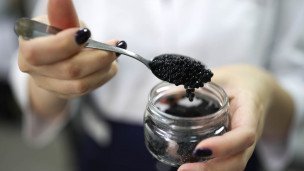 Девушка держит на ложке черную икру
