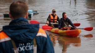 Сотрудник МЧС России и люди в лодке на затопленной улице.