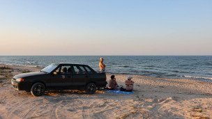 Горожане во время отдыха на пляже рядом с машиной