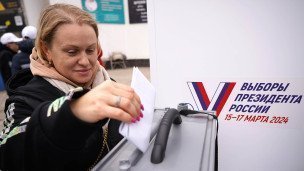 Женщина опускает в урну бюллетень на голосовании