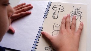 Незрячий ребёнок читает с помощью рук книгу 