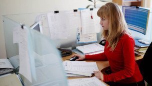 Офисная сотрудница за компьютером в окружении документов