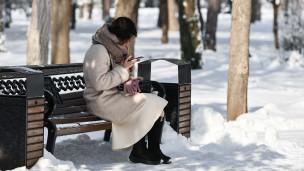 Девушка с телефоном в парке сидит на скамейке