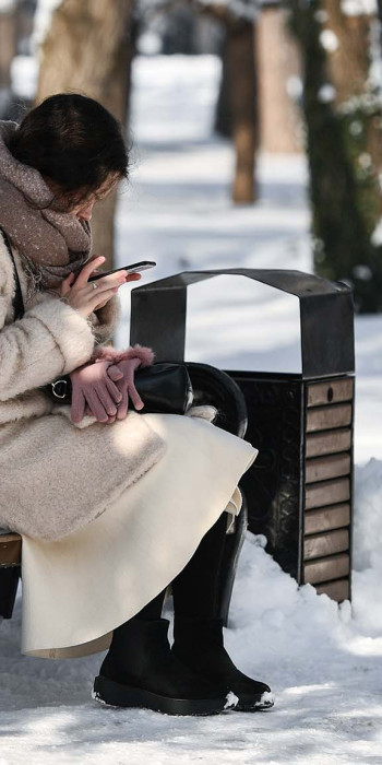 Девушка с телефоном в парке сидит на скамейке