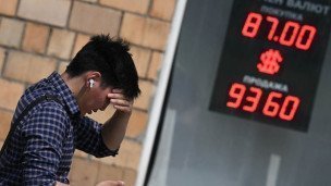 Мужчина беспокойно смотрит в телефон на фоне табло с курсом валют