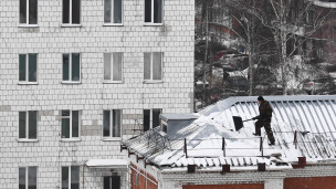 Рабочий сбрасывает снег с крыши дома 