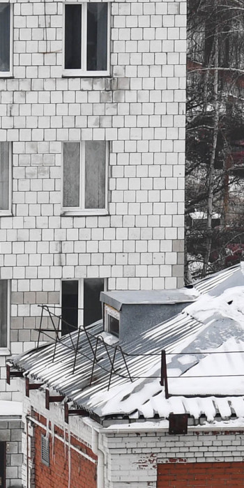 Рабочий сбрасывает снег с крыши дома 