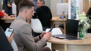Мужчина в коворкинге сидит с телефоном в руках перед ним на столе ноутбук и планшет 