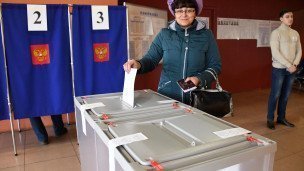 Женщина опускает бюллетень в урну во время голосования