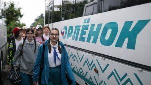 Улыбающиеся дети идут рядом с автобусом на котором написано Орленок