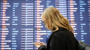 Женщина со смартфоном у информационного табло международного терминала аэропорта 