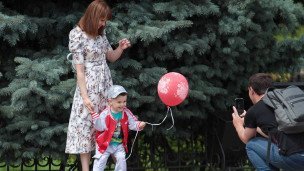Семья с маленьким ребенком фотографируется в парке