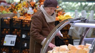 Пожилая женщина выбирает сыр в супермаркете 