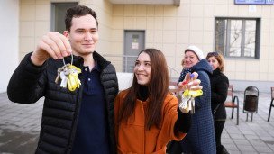 Молодые люди с ключами в руках возле многоэтажного жилого дома 