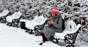 Женщина с телефоном сидит на скамейке в парке 