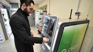 Молодой человек проводит денежные операции с помощью стационарного банкомата "Сбера"