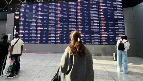 Люди у электронного табло с информацией о вылетах в аэропорту