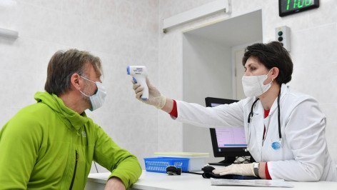 Врач измеряет температуру мужчине перед вакцинацией