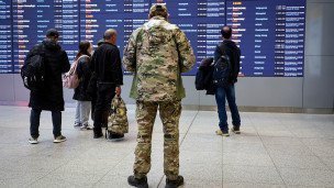 Пассажиры у информационного табло терминала аэропорта, мужчина в военной форме на переднем плане