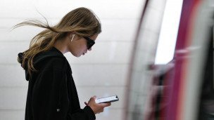 Девушка в метро на фоне прибывающего поезда смотрит в телефон