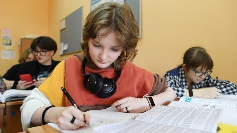 Школьница сидит за партой и выполняет задание в тетради
