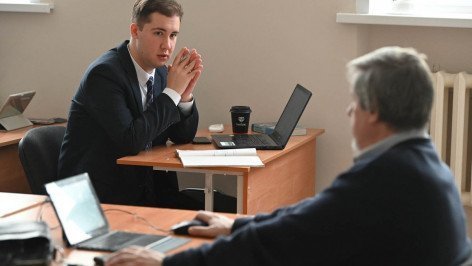 Студент в аудитории за ноутбуком разговаривает с профессором 