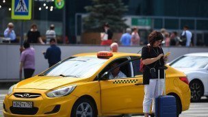 Женщина с чемоданом и телефоном в руках у такси