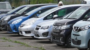 Посетительница осматривает выставленные на продажу подержанные легковые автомобили 