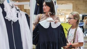 Женщина выбирает школьную форму с ребенком в магазине