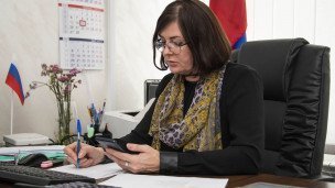 Женщина в кабинете подписывает документы рядом российский флаг