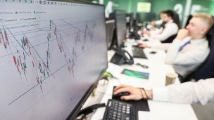 Сотрудники в офисе банка за компьютерами на экране которых графики