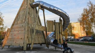 Современная деревянная детская площадка, мальчик на новой горке на фоне жилого дома