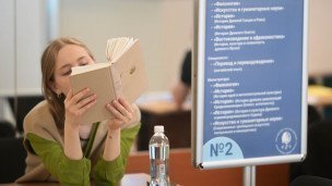 Девушка с учебником у стенда "института филологии и истории" 