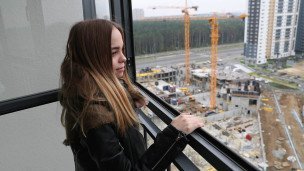 Девушка смотрит в окно из новой квартиры