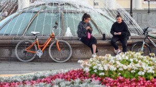 Две девушки сидят на краю фонтана рядом стоят два велосипеда