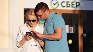 Пара смотрит в телефон около отделения Сбера