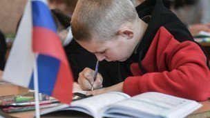 Школьник за партой пишет на столе стоит флаг России