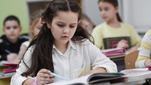 Школьница за партой изучает учебник