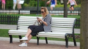 Женщина с телефоном в руках на скамейке в парке