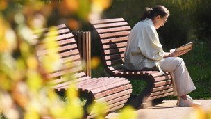 Пожилая женщина читает книгу на скамейке