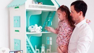 Мужчина с ребенком на руках рассматривают игрушечный домик