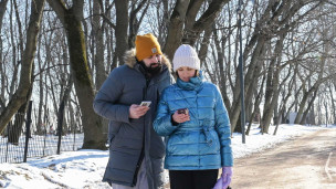 Женщина и мужчина в парке смотрят в экраны смартфонов