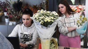 Сотрудницы цветочного магазина, одна за ноутбуком, вторая с букетом в руках