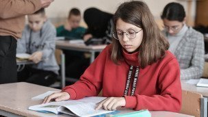 Девочка в классе за партой читает учебник