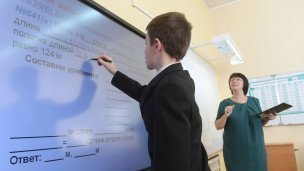 Ученик выполняет задание возле интерактивной доски на заднем плане учительница